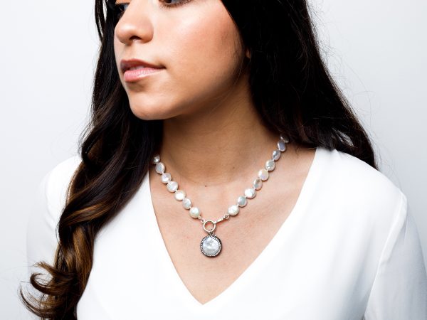 Hispanic woman with long dark hair wearing a v-neck white shirt and a pearl necklace with a pearl pendant